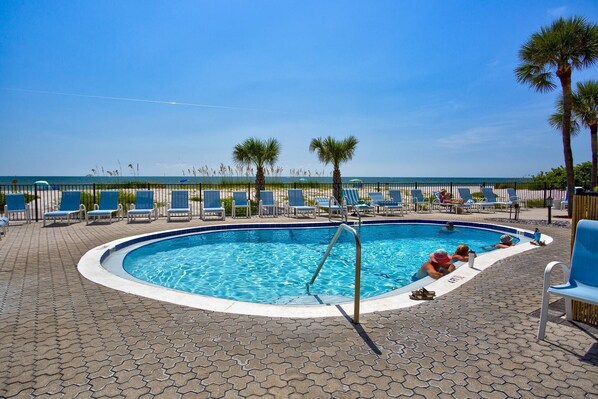Piscina con sillas de descanso y palmeras, con vista a una playa.