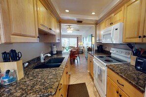 Una cocina con encimeras de granito, armarios de madera, estufa, microondas y un comedor con una silla y una mesa.