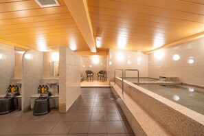 A modern spa with a large hot tub, a sauna, and a shower area with benches. - Shinsaibashi ARTY Inn (Osaka)