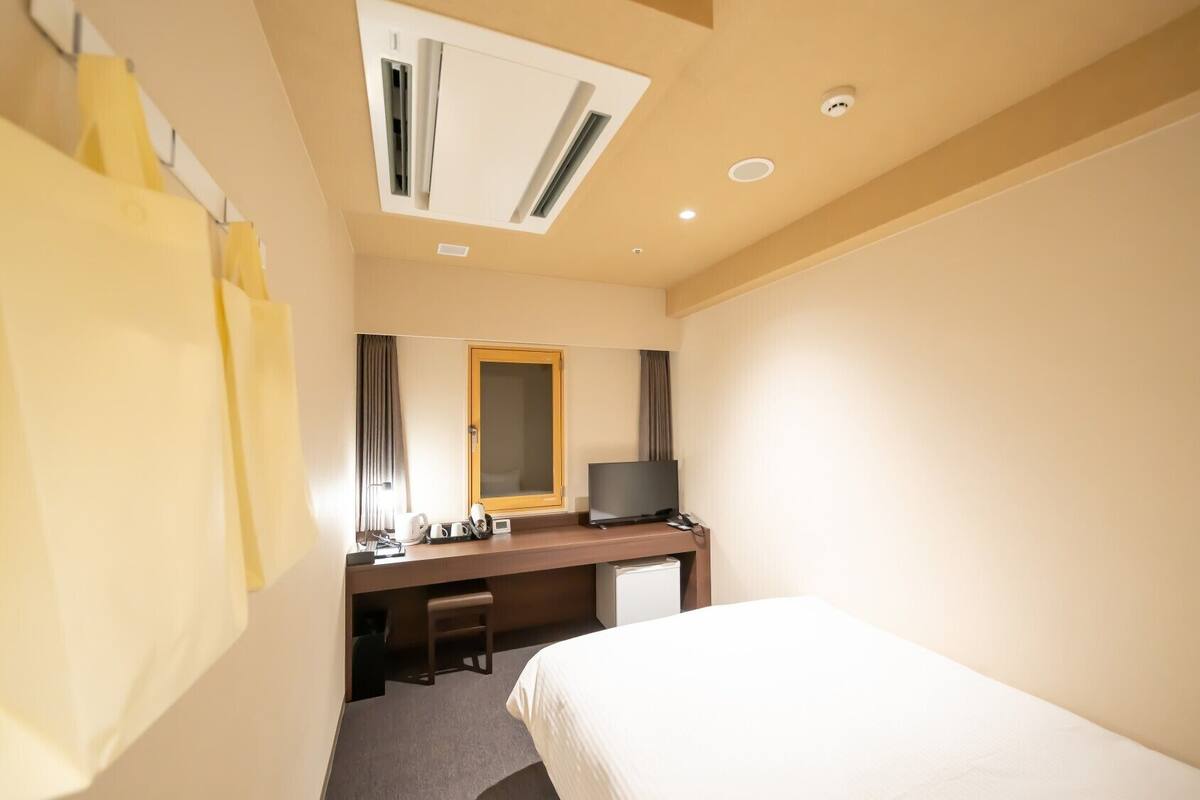 A hotel room with a bed, a desk with a television, a mirror, and a window with curtains.
