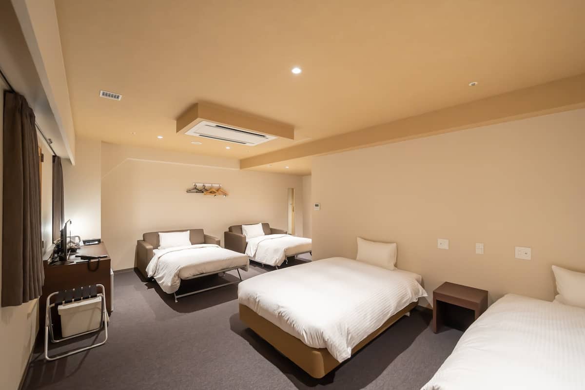 A hotel room with two beds, a desk, a chair, a small table, and a wardrobe.