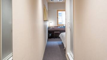 A narrow hallway leading to a bedroom with a window, a desk, and a chair.