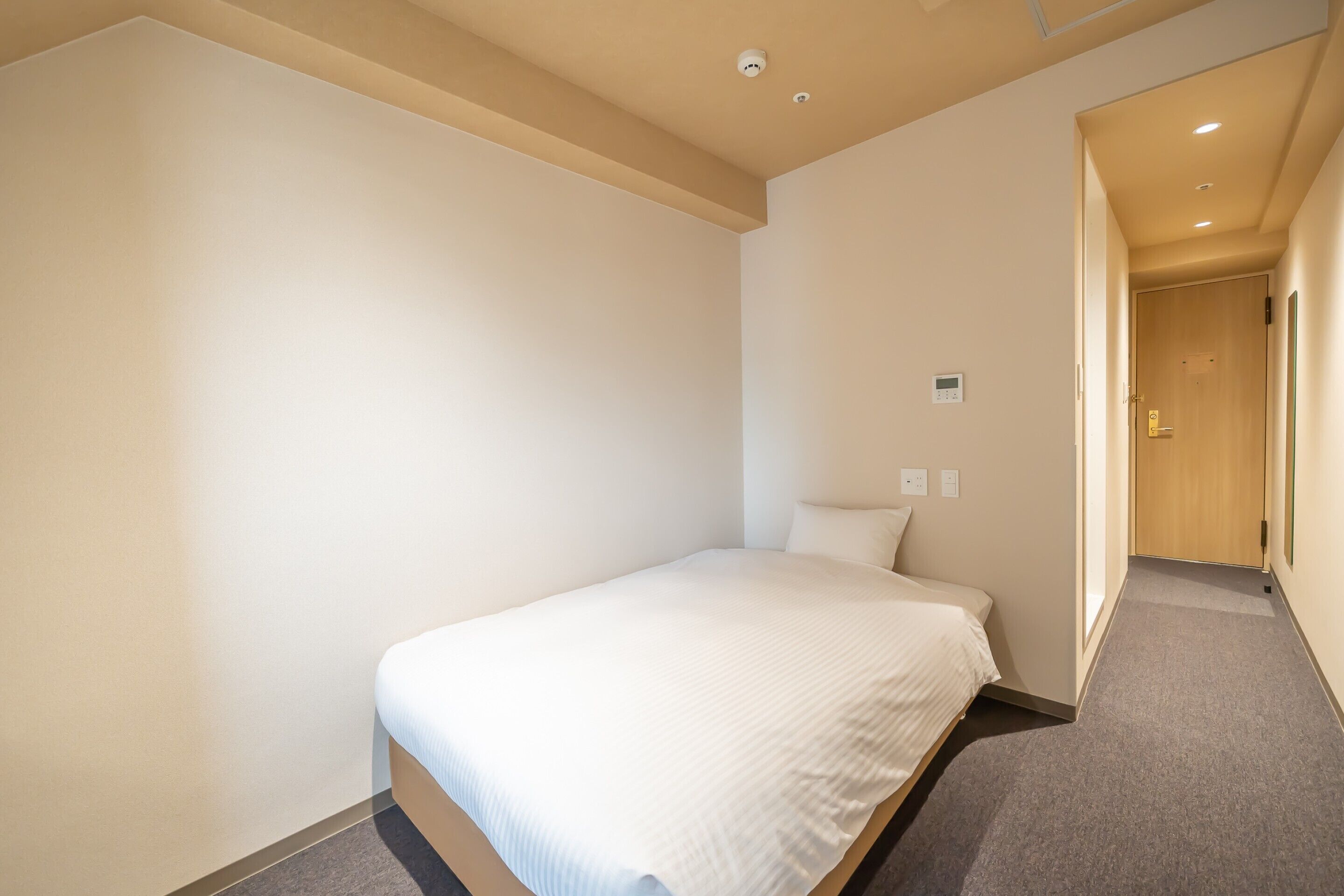 A single bed in a room with a carpeted floor and a wooden door in the background.
