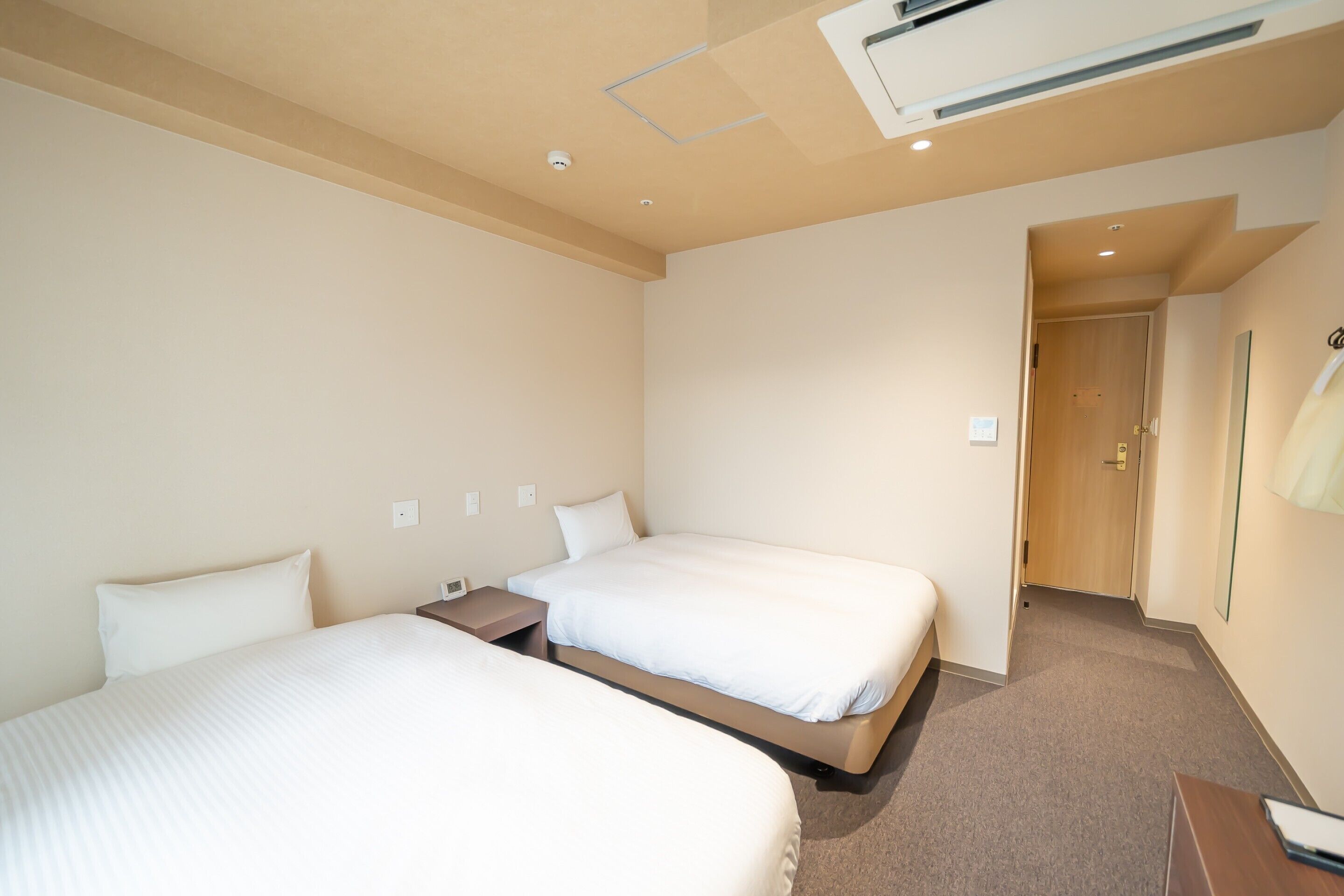 Une chambre d’hôtel avec deux lits, une porte en bois, une table de chevet et un climatiseur fixé au mur.