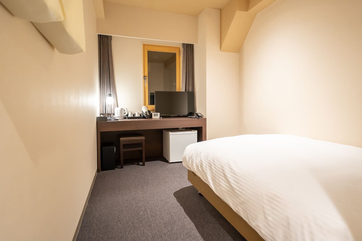A hotel room with a bed, a desk with a computer, a television, and a small refrigerator.