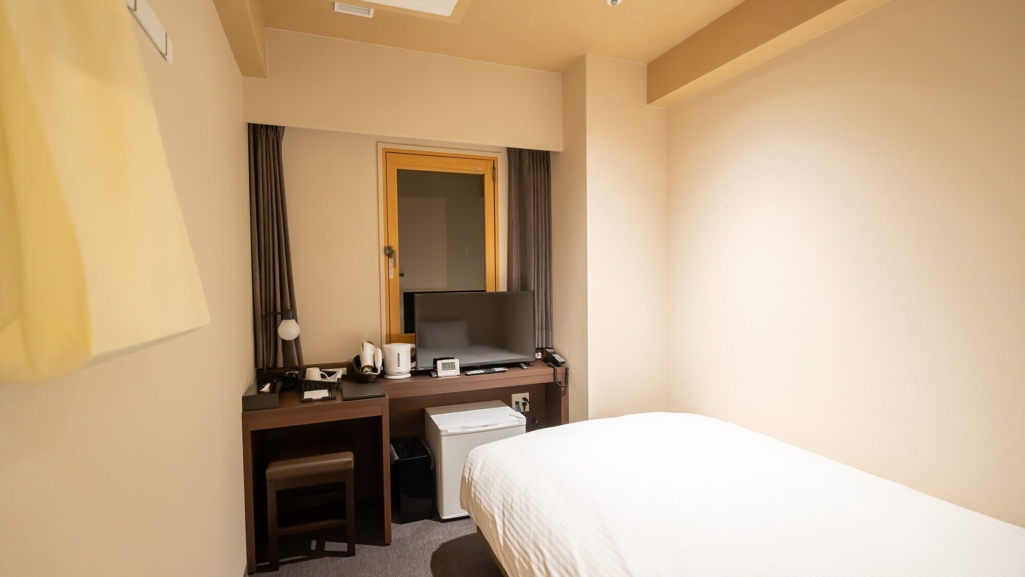A hotel room with a bed, a desk with a computer, a telephone, and a small stool.
