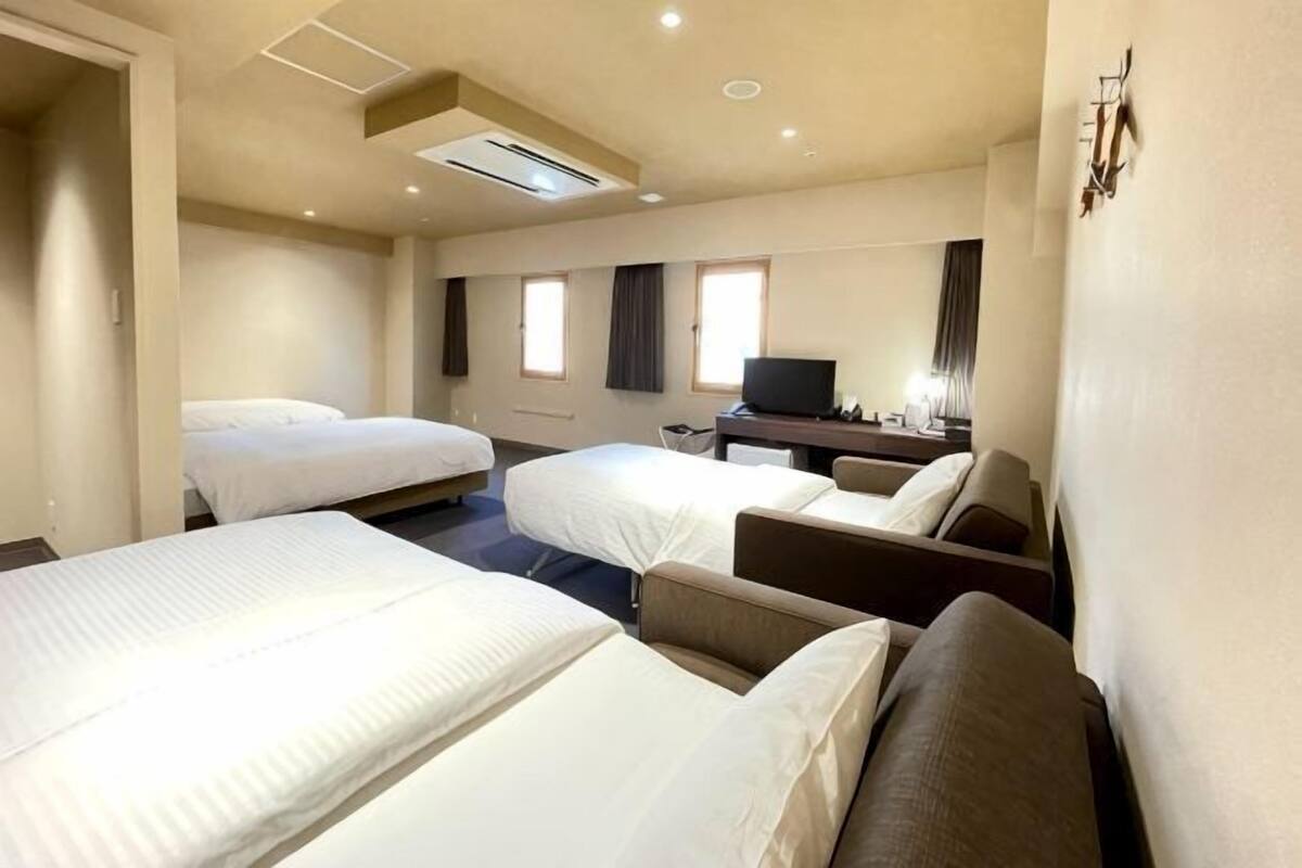A hotel room with three beds, a desk, a chair, and a TV.