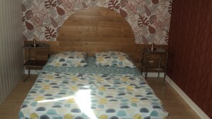 Une chambre à coucher avec une tête de lit en bois, un lit recouvert d’une couvre-lit à motifs, deux tables de chevet et un papier peint à motifs floraux.