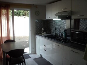 A modern kitchen with white cabinets, a black countertop, and a stove. There is a window with curtains, a clock on the wall, and a door leading outside.