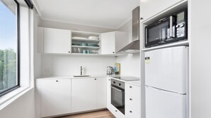 Een moderne keuken met witte kastjes, een inbouwoven, een magnetron en een raam met uitzicht op de omgeving.