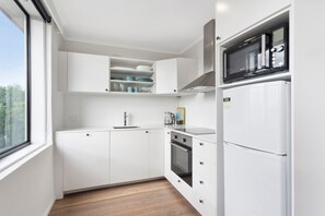 Eine moderne Küche mit weißen Schränken, einem eingebauten Backofen, einer Mikrowelle und einem Fenster mit Blick ins Freie.