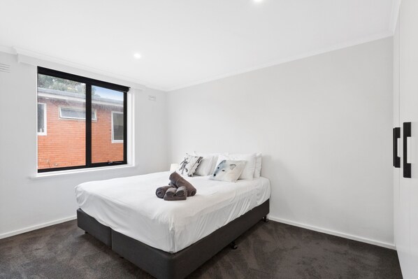 A modern bedroom with a large window, a bed with white linens, and a grey upholstered headboard.
