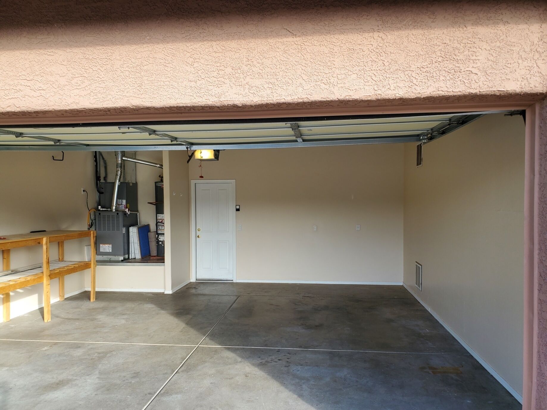 Ett garage med ett betonggolv, en träbänk och en vit dörr.