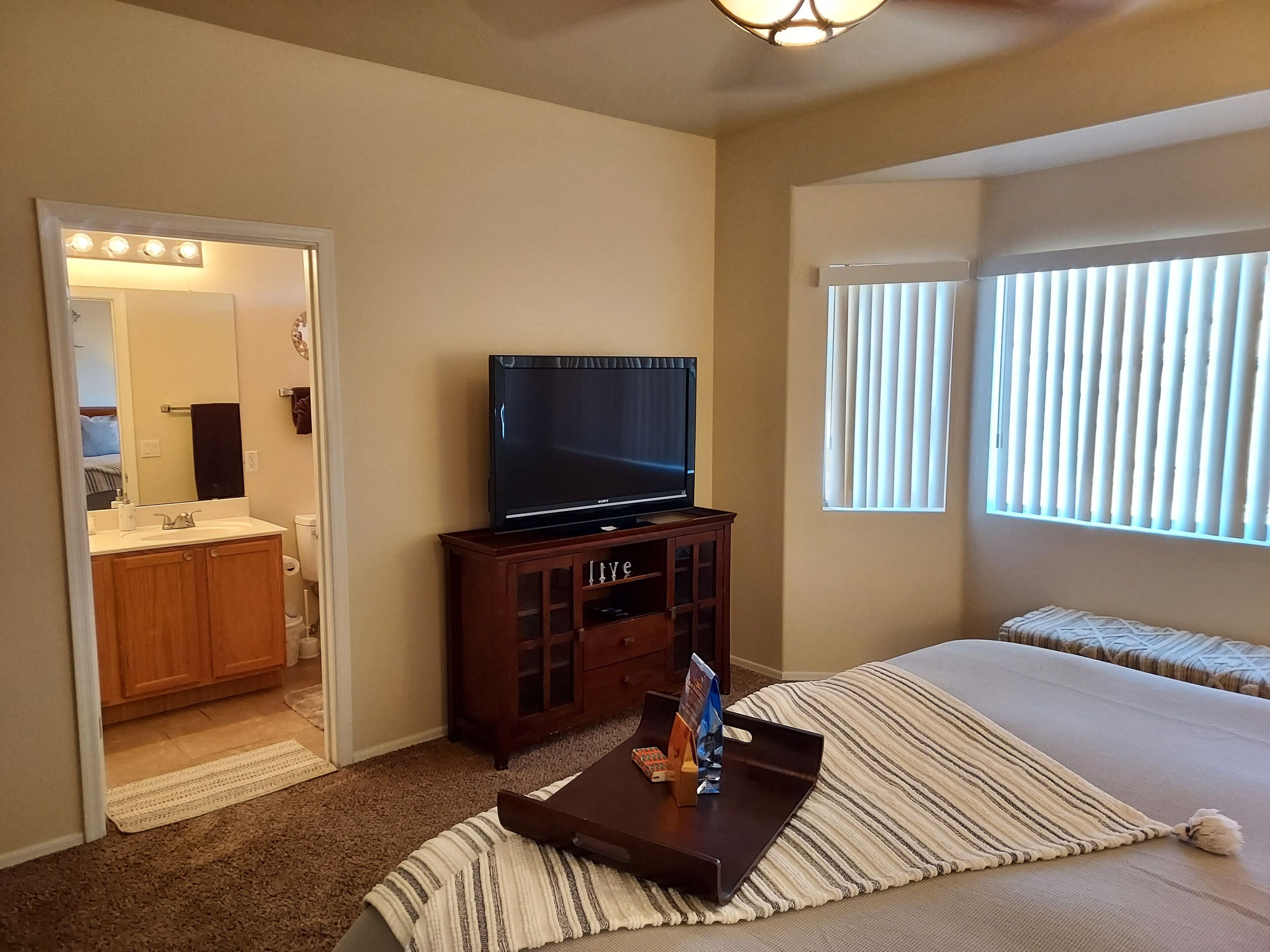Ein Hotelzimmer mit Fernseher auf einem Holztisch, einem Bett mit gestreifter Bettwäsche, einem Fenster mit Jalousien und einem durchgegangenen Türspalte sichtbaren Badezimmer.