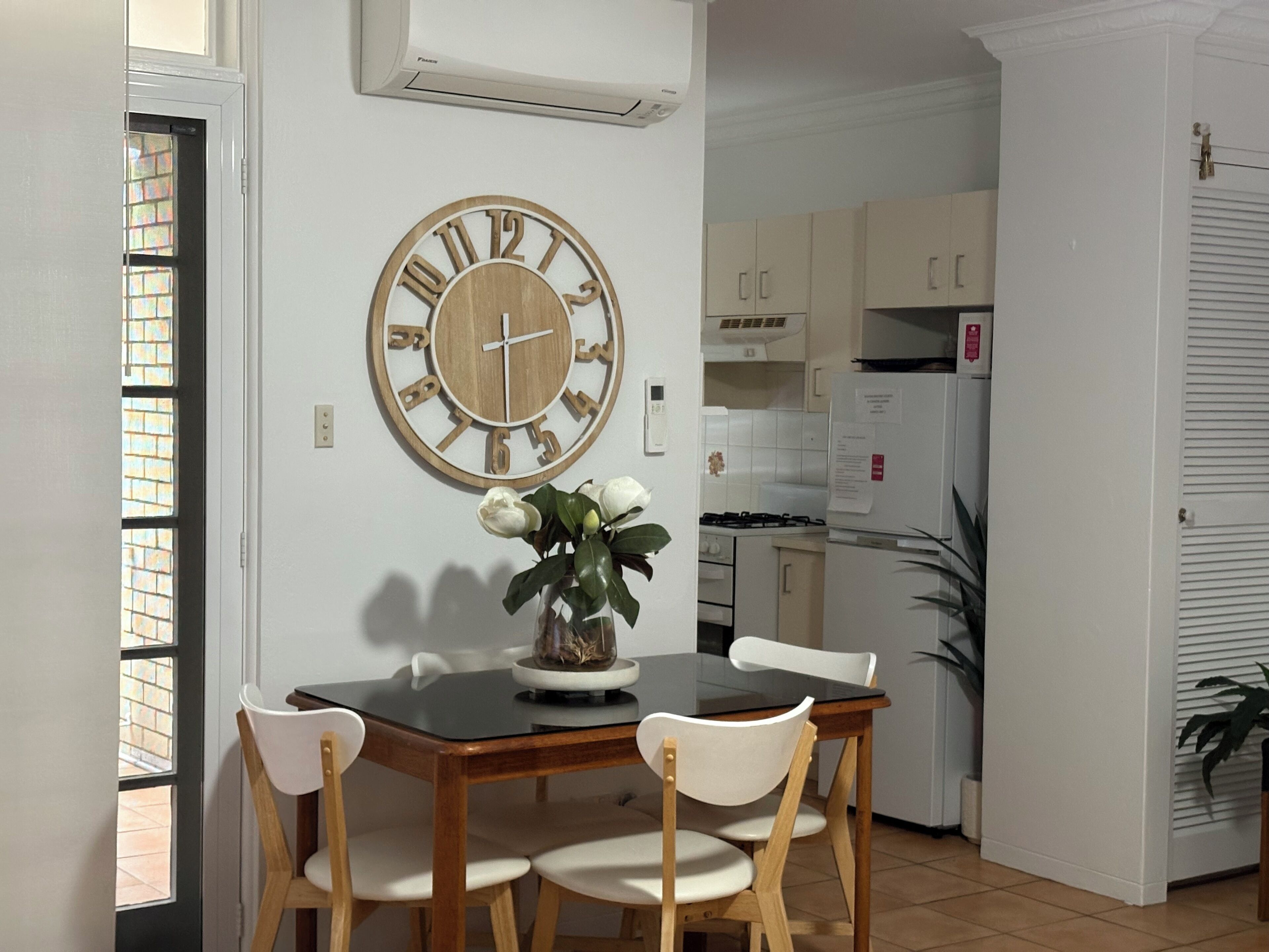 A dining area with a wooden table, four chairs, and a wall clock.