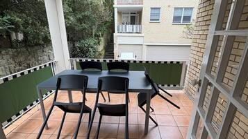 A covered patio area with a table and chairs, a green railing, and a view of a residential building.