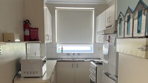 Eine kleine Küche mit weißen Schränken, einem eingebauten Backofen und einem Fenster mit Jalousie.