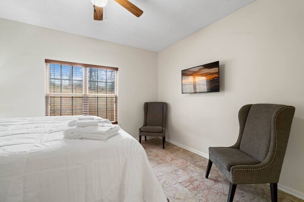 Een hotelkamer met een bed, een stoel, een raam met jaloezieën en een schilderij aan de muur.