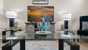 Een moderne woonkamer met een glazen salontafel, twee lampen, een televisie en een bord met de tekst 'welcome'.