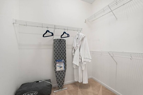 A small, bright room with a drying rack, an ironing board, and a bag on the floor.
