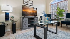 Een moderne woonkamer met een open haard, een glazen salontafel en een grote televisie.