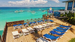 A wooden deck with white lounge chairs and blue cushions, overlooking turquoise waters with boats. - Zenobia Beach Resort (Nungwi)