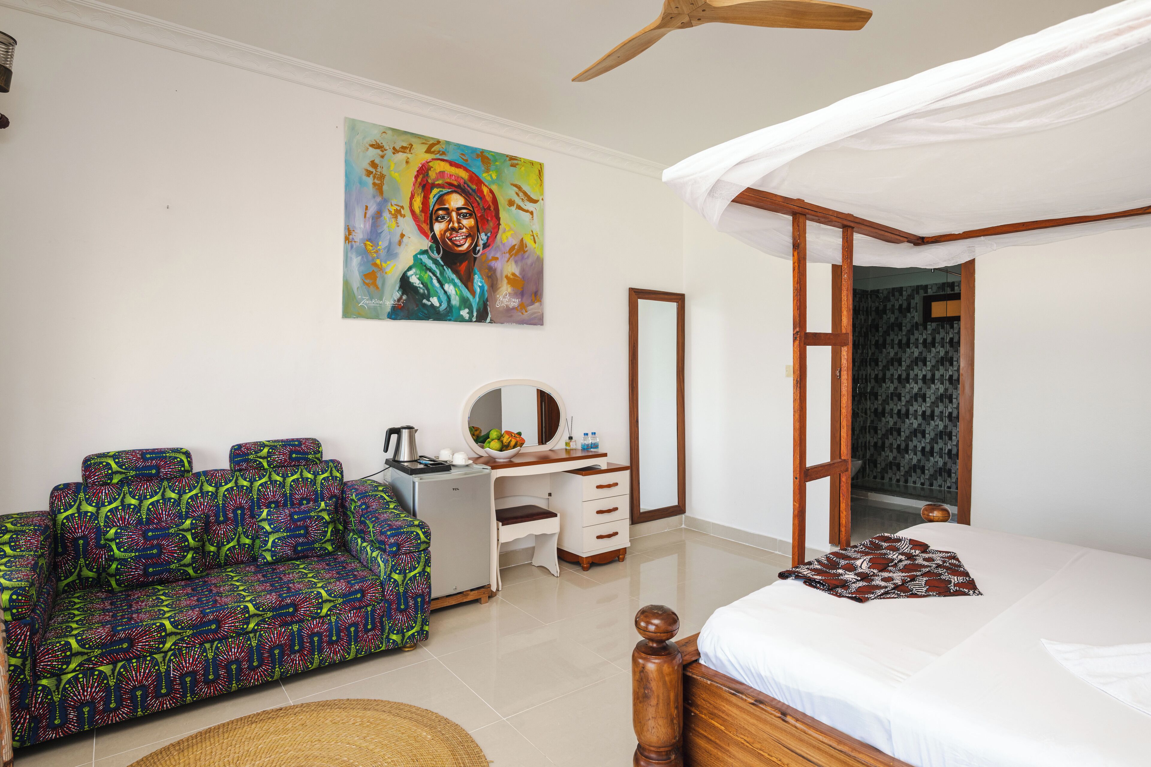 A bedroom with a bed, a sofa, a desk, and a mirror.