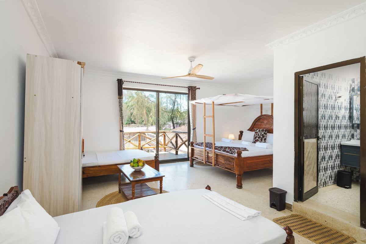A hotel room with a large bed, a smaller bed, a balcony with a view, and a ceiling fan.