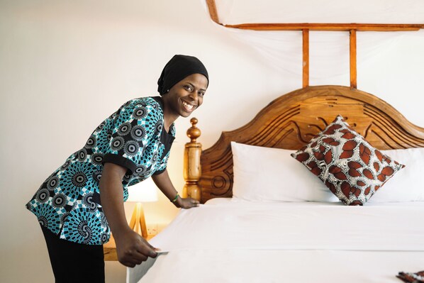 Uma pessoa arrumando uma cama com cabeceira de madeira e almofadas estampadas em um quarto com design simples e clean.