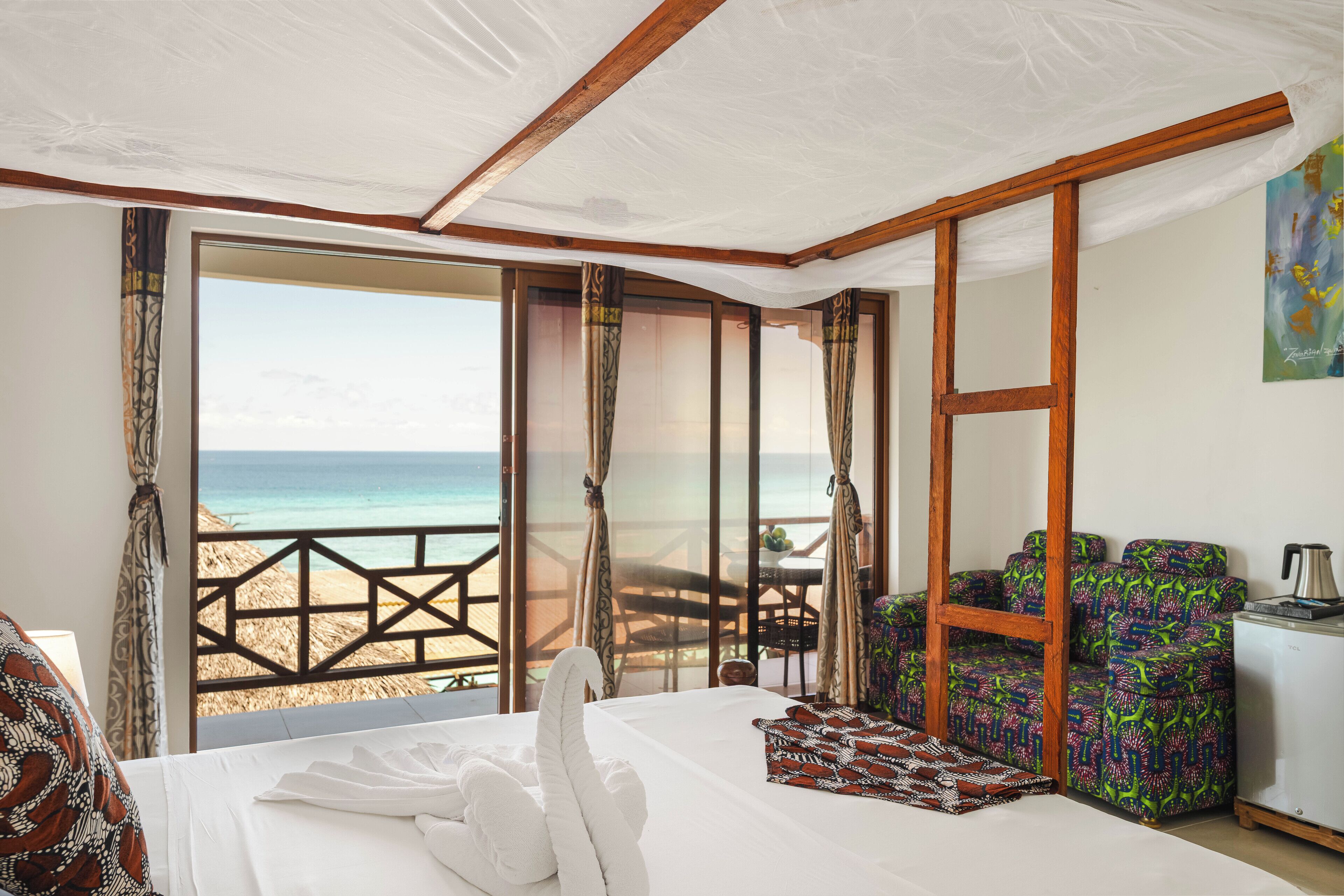 A hotel room with a bed, a seating area with a table and chairs, and a view of the beach.