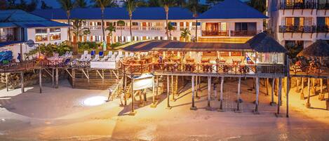 A beachfront resort with a pool area, outdoor seating, and a bar.