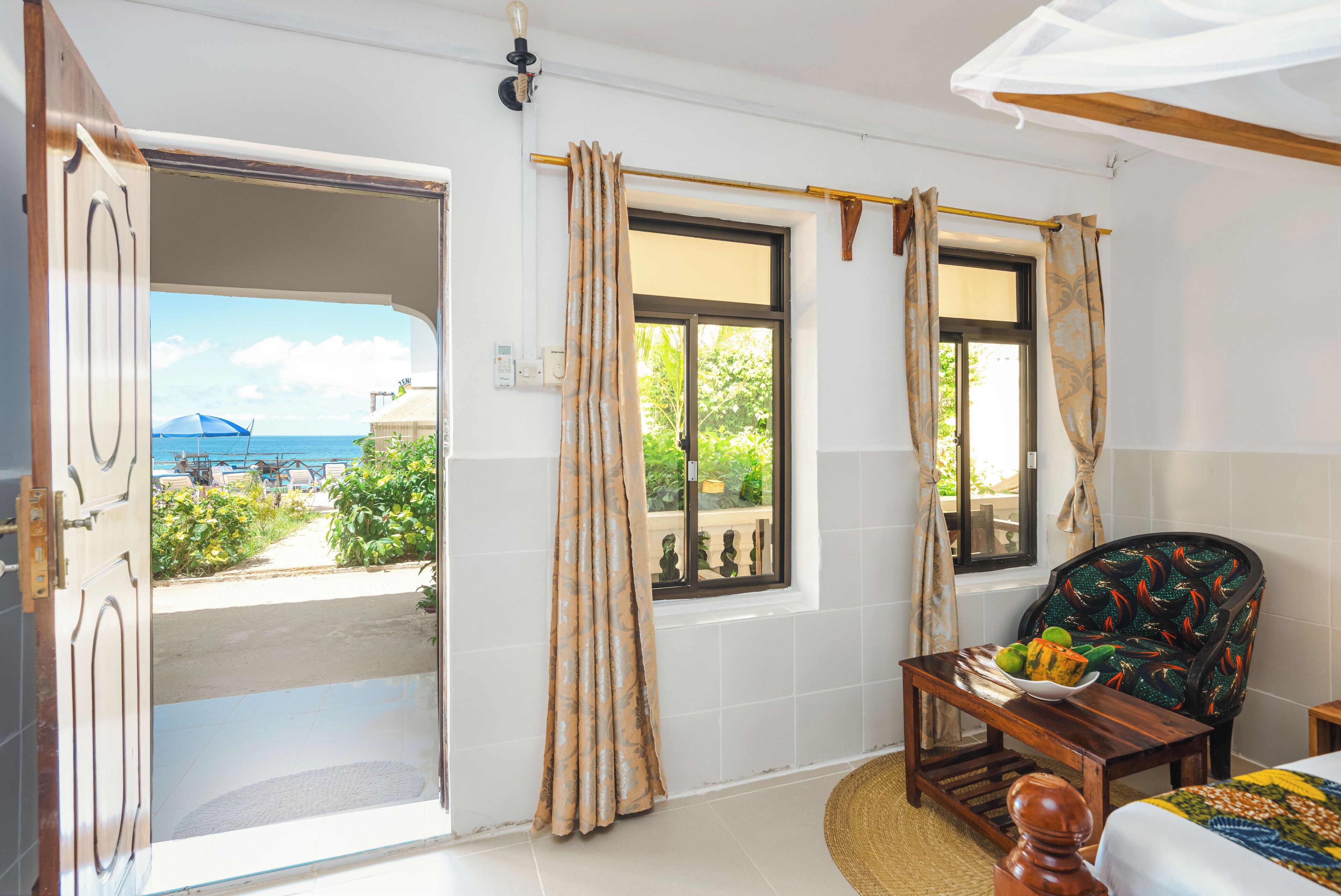 A room with a view of the sea, a chair, a table with fruit, and a bed.