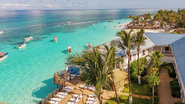 A resort with a beach, clear turquoise waters, and a dock with boats. - Zenobia Beach Resort (Nungwi)