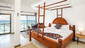 A four-poster bed with a canopy, a wooden headboard, and a view of the ocean through a balcony door. - Zenobia Beach Resort (Nungwi)