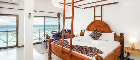 Een hemelbed met een baldakijn, een houten hoofdbord en uitzicht op de oceaan door een balkondeur.