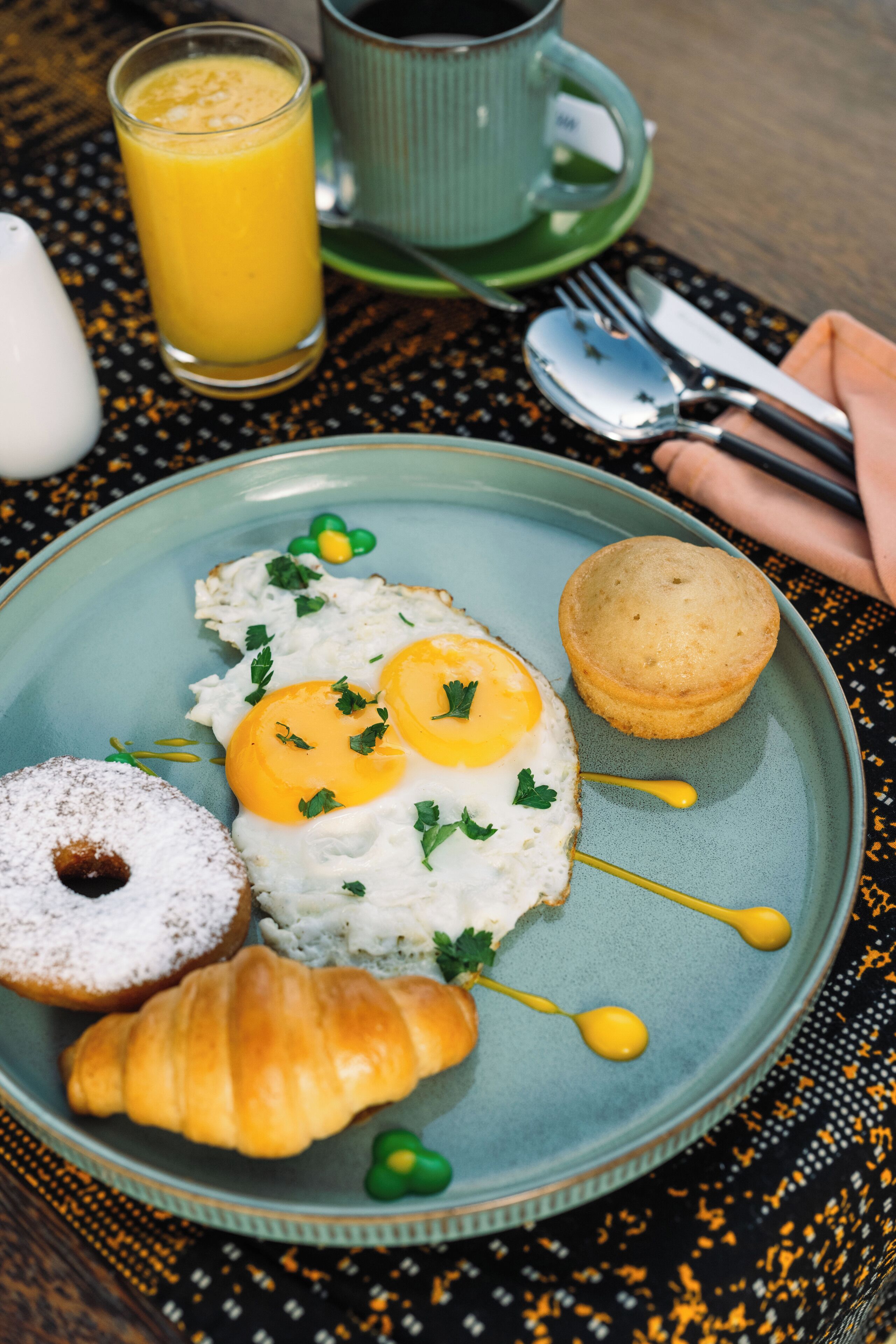 A breakfast plate with eggs, a muffin, a croissant, and a glass of orange juice on a table.