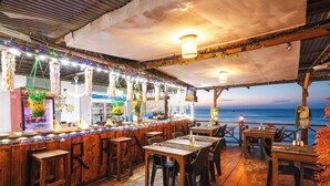 A wooden bar area with a view of the ocean, featuring a bar counter, stools, and tables. - Zenobia Beach Resort (Nungwi)