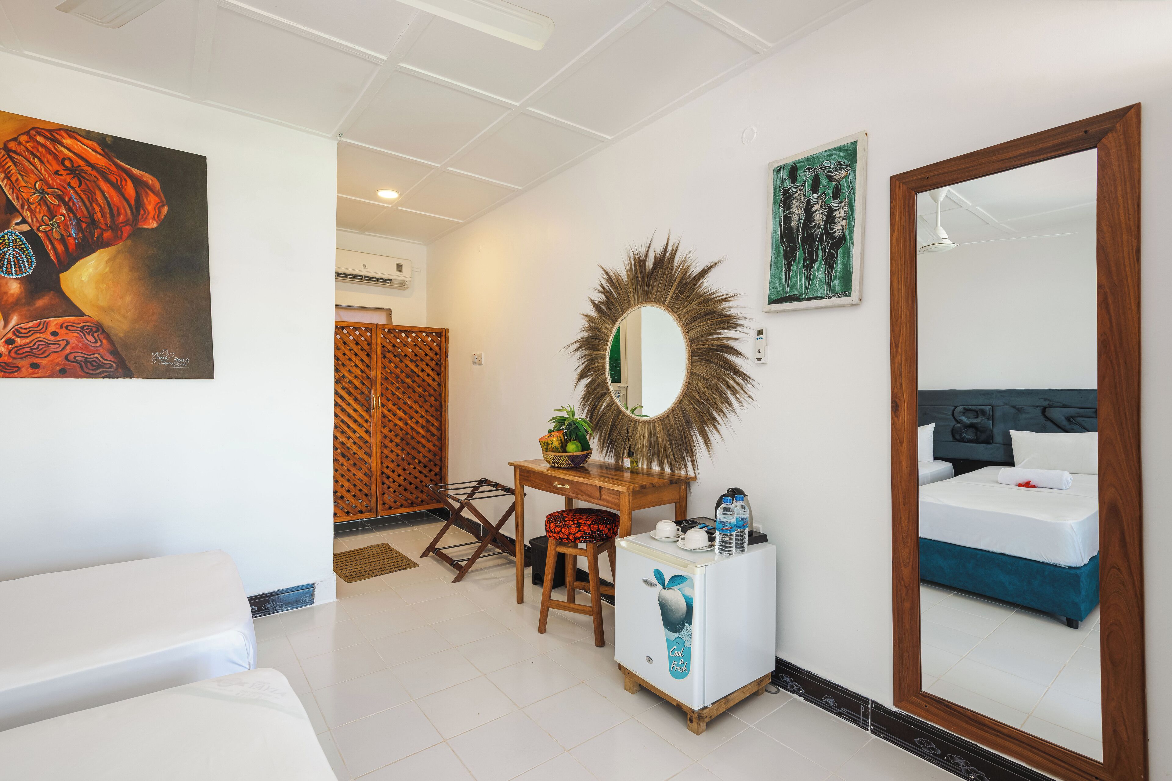 Una habitación de hotel con cama, escritorio con espejo, un refrigerador pequeño y una silla.