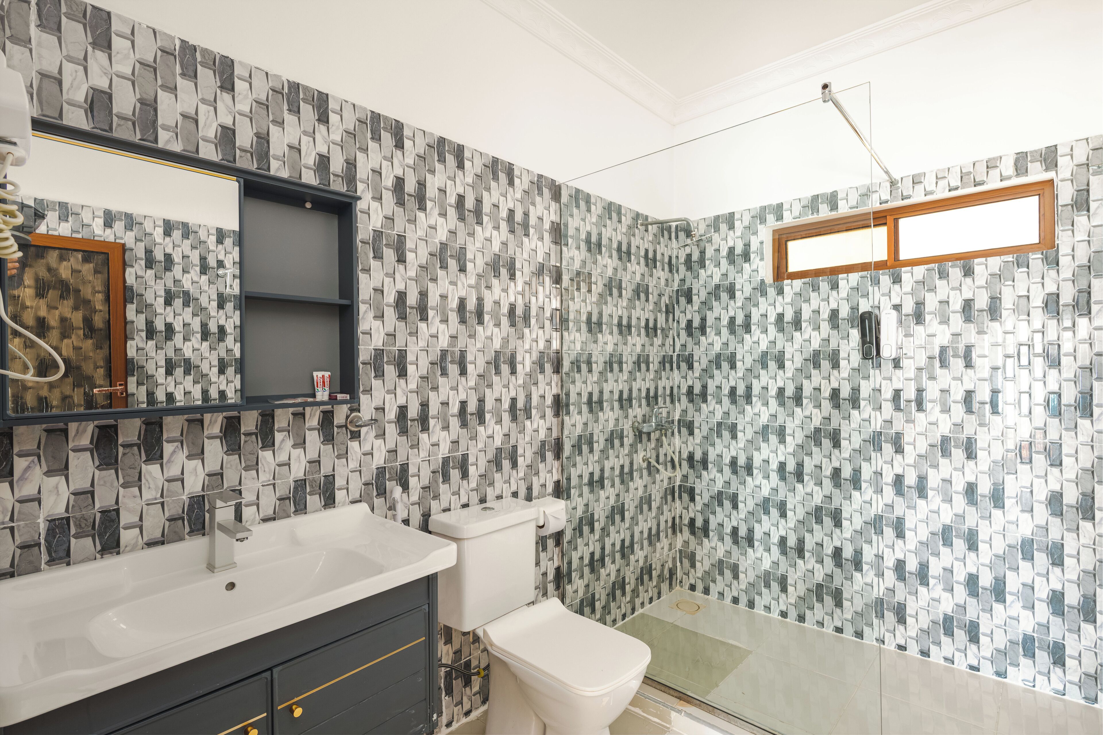 Un baño con pared de mosaicos, un lavamanos blanco, un inodoro y una zona de ducha.