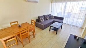 A living room with a wooden dining table, a grey sofa, a black coffee table, and an air conditioning unit on the wall. - License to Chill Apartment (Larnaca)