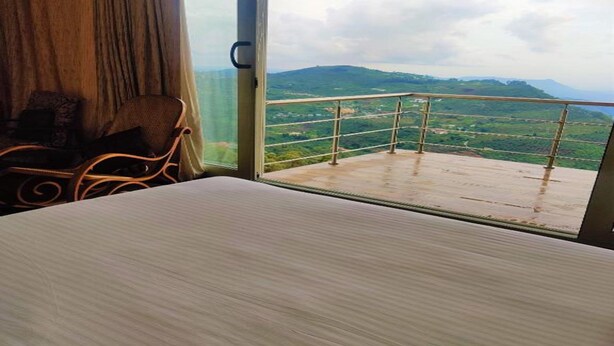 Ein Zimmer mit Bett, einem Sessel und einem Balkon mit Blick auf grüne Hügel.