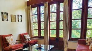 Ein Zimmer mit einem Glastisch, zwei roten Sofas, einem gemusterten Teppich und großen Fenstern mit Vorhängen.