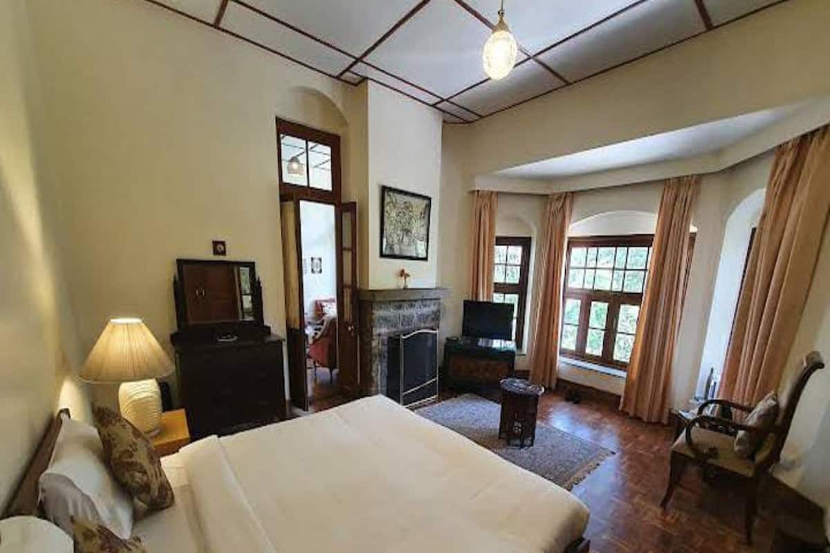 Ein geräumiges Schlafzimmer mit einem großen Bett, einem Fernseher, einem Kamin und Blick ins Freie durch große Fenster.