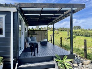 Une terrasse couverte, aménagée avec du mobilier d’extérieur, un chien et une vue sur un paysage verdoyant.
