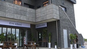 En byggnad med en skylt som visar en dykskola och ett café, med en fasad av sten, utomhusplatser och krukväxter.