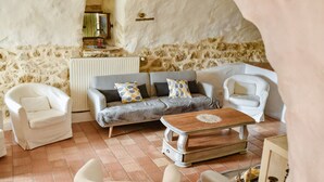A cozy living room with a stone wall, a grey sofa with patterned cushions, a wooden coffee table, and white armchairs. - Magnificent private Mas Ardechois with swimming pool (Labastide-de-Virac)