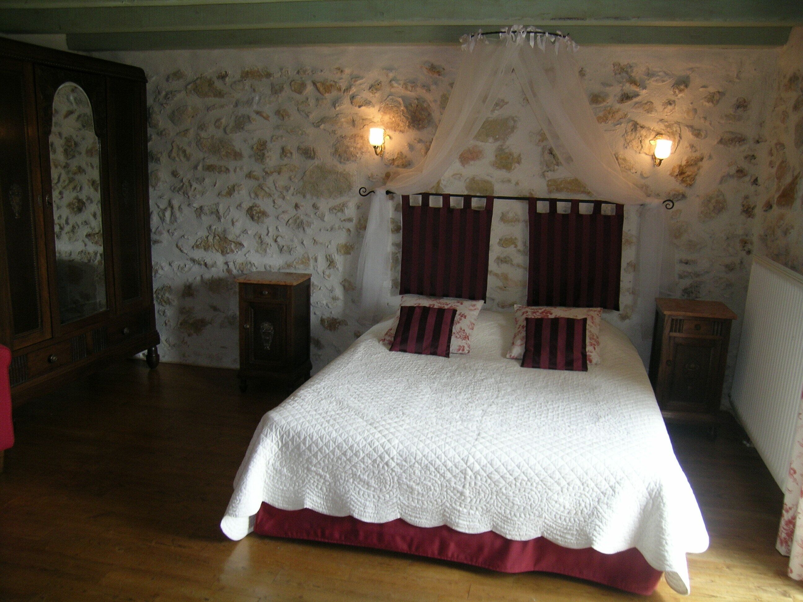 Een slaapkamer met een groot bed, twee nachtkastjes, een houten garderobe en een wand met een steenmotief.