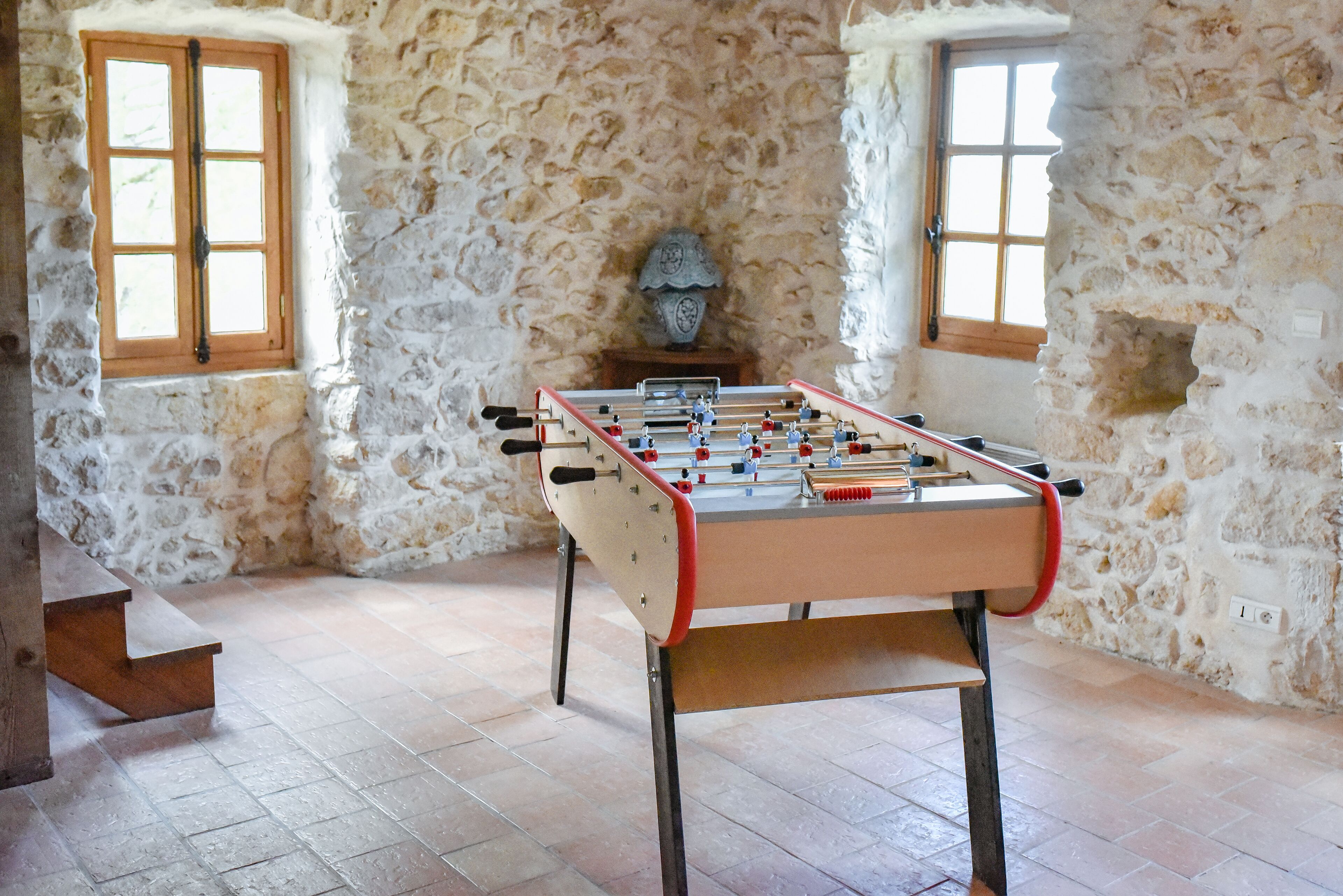 Ein Tischkicker in einem Raum mit Steinwänden und zwei Fenstern.