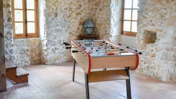 Ein Tischkicker in einem Raum mit Steinwänden und zwei Fenstern.