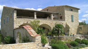 A stone building with a balcony, arched entrance, and a small garden area with potted plants. - Magnificent private Mas Ardechois with swimming pool (Labastide-de-Virac)